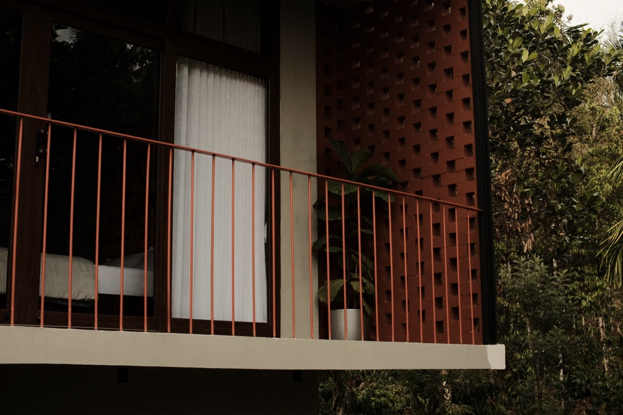 Rust-red balcony railing against the perforated terracotta jali screen