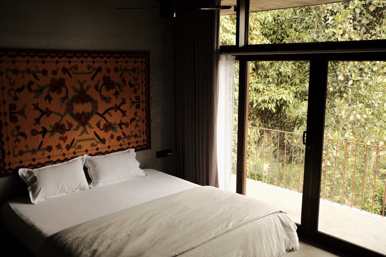 A bedroom opening through glass doors onto a balcony and green canopy
