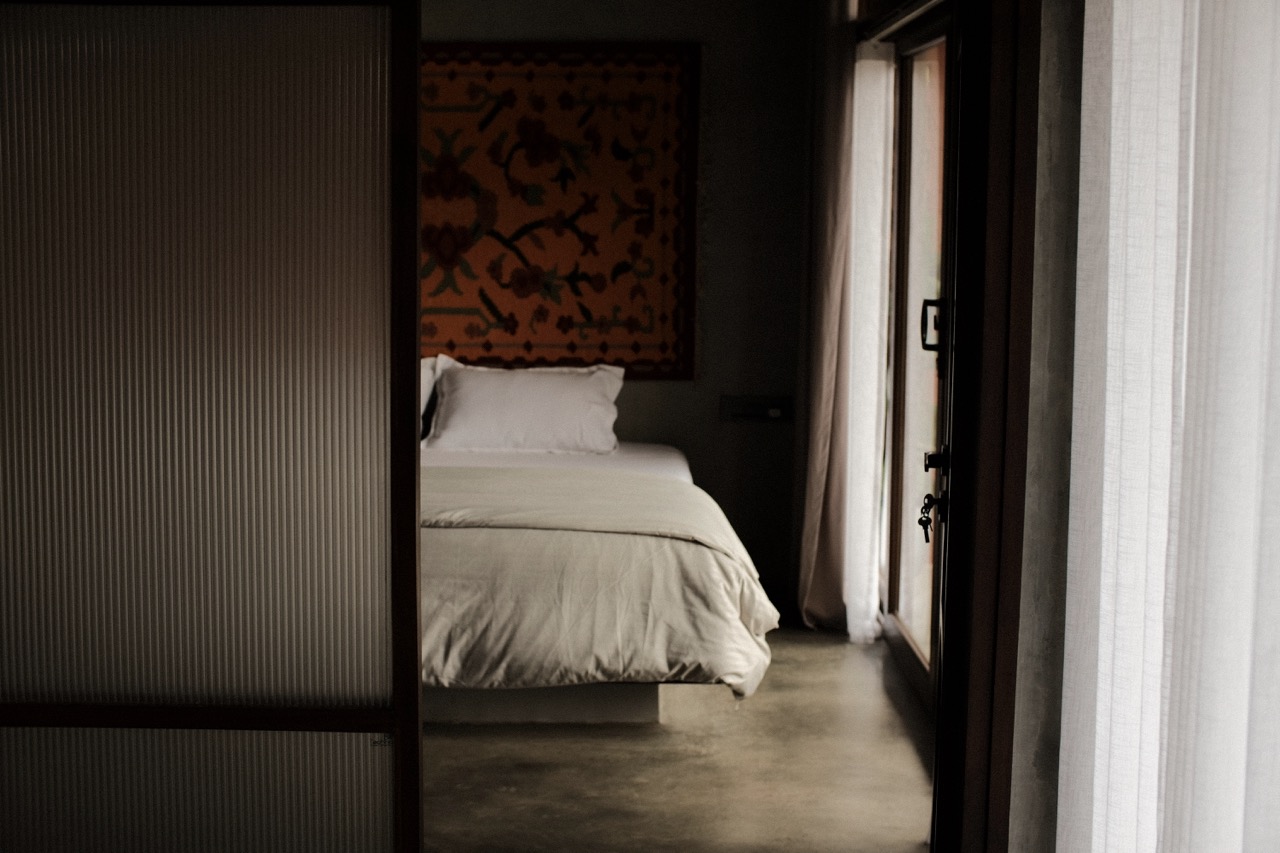 A bedroom seen through the doorway, light falling across the concrete floor