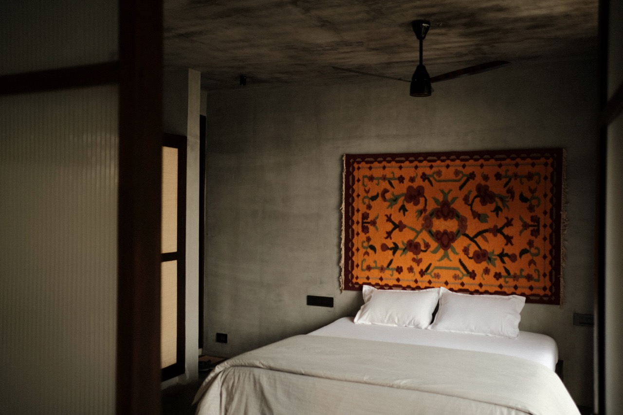 A bedroom with a woven kilim hung above the bed against a lime-washed concrete wall