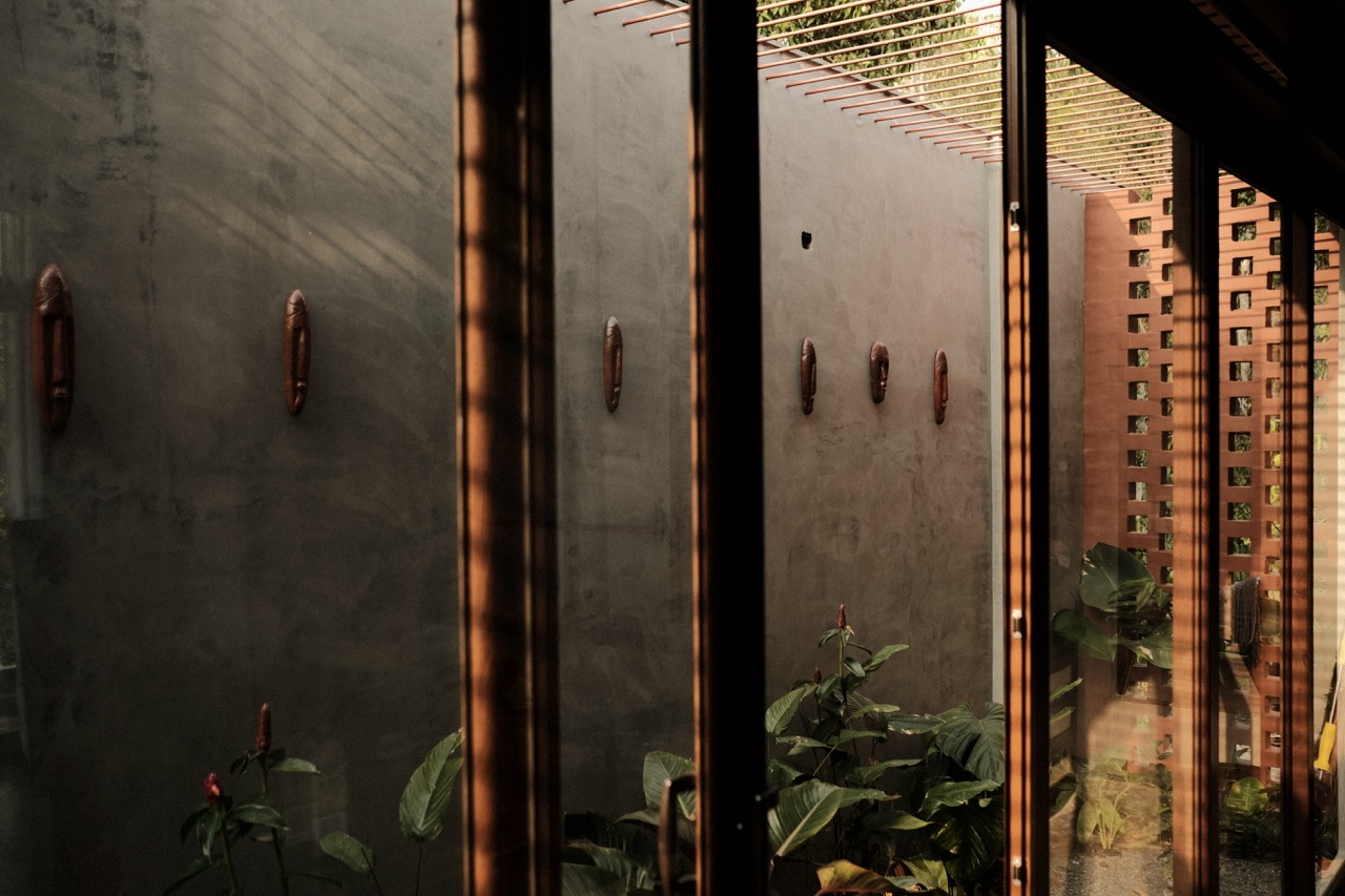 Carved wooden masks arranged on a lime-washed wall, seen through glazing with a jali screen beyond