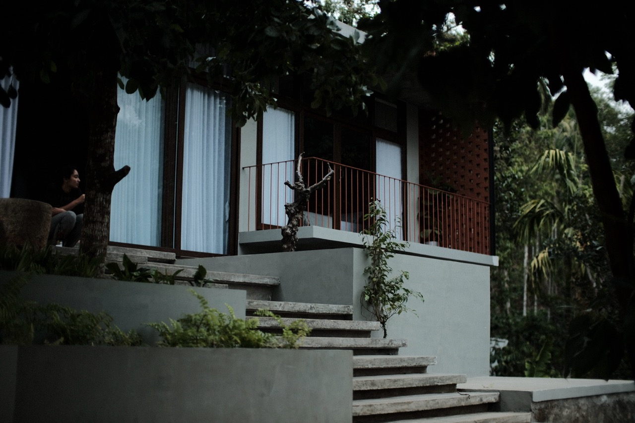 A guest sitting quietly on the verandah steps in the evening, framed by trees